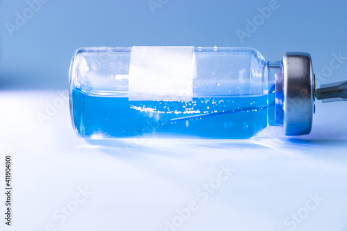A vial with a blue vaccine with a syringe needle inside