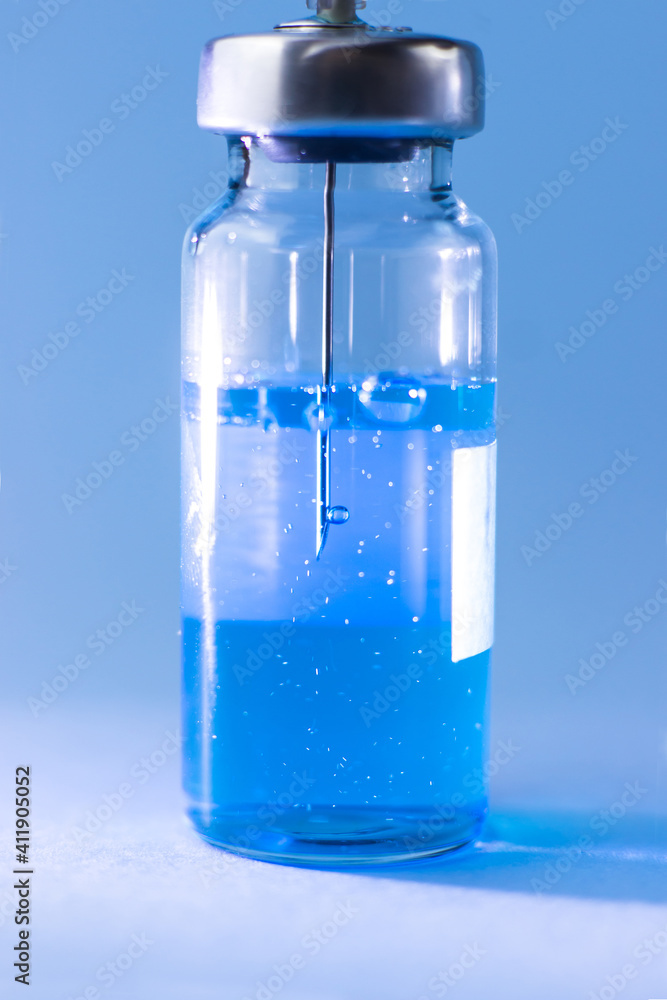 A vial with a blue vaccine with a syringe needle inside