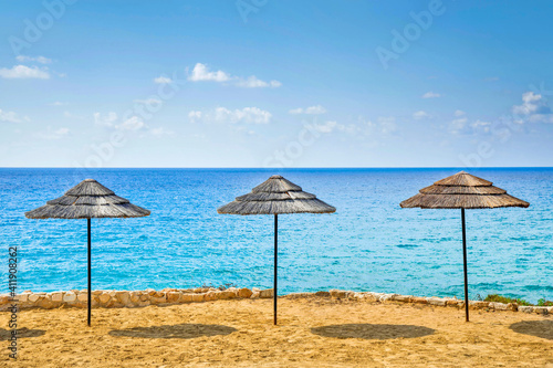 three wooden umbrellas  on a sandy beach,beautiful viiew ,sunny day © andrijosef