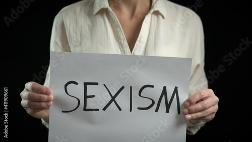 Woman against sexism. Female with a sexism poster on a black background.