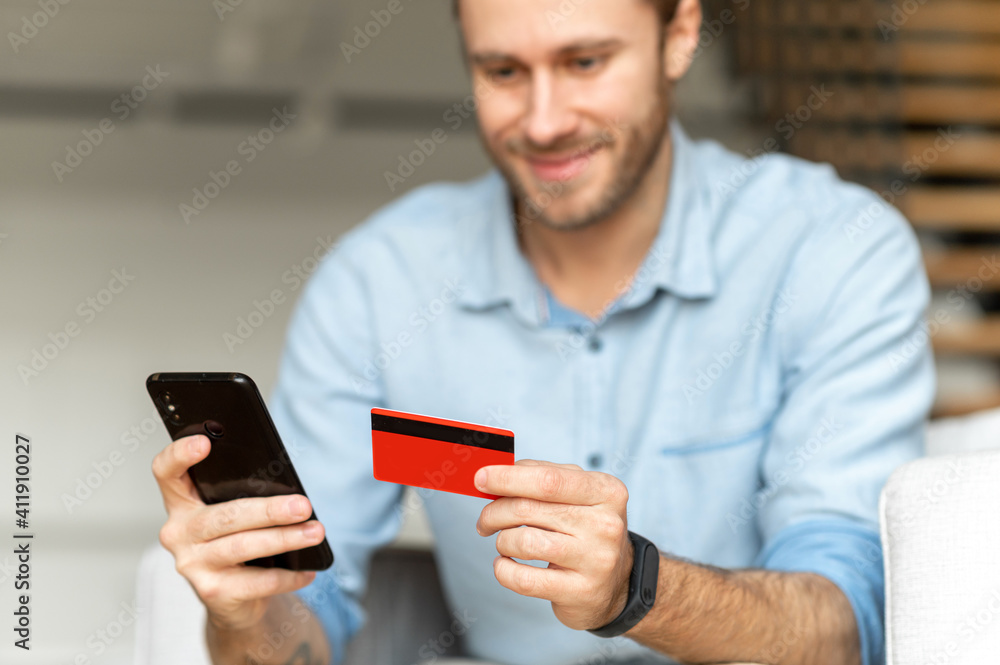 Close-up a credit card and a smartphone in male hands. Cheerful man typing a credit card number on her mobile phone, buying items from online application, transferring money, internet banking concept Close-up a credit card and a smartphone in male hands. Cheerful man typing a credit card number on her mobile phone, buying items from online application, transferring money, internet banking concept