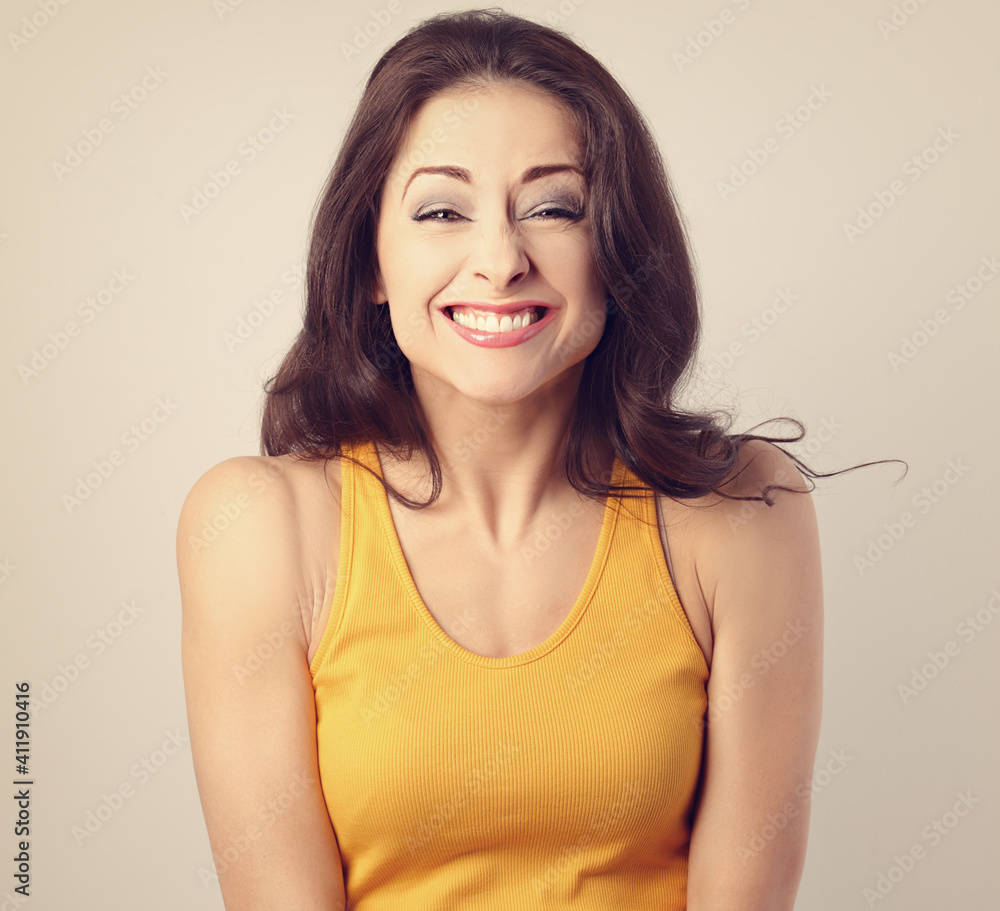 Fototapeta premium Beautiful happy toothy chuckling woman with brown hair in casual yellow t-shirt looking happy on studio background with empty copy space. Closeup toned