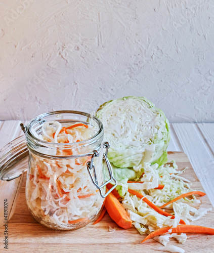 Homemade sauerkraut with carrots in a glass jar on wooden table. Fermented vegetables. Vegetarian vegan food. Sauercraut- cut, fermented cabbage, german and russian style cuisine.