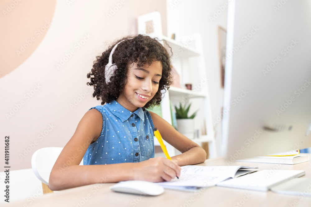Clever little multiracial girl fill in exercise book, watching video classes, training for an exam, researching topic for essay, studying on the distance, doing homework. Studying and technology Clever little multiracial girl fill in exercise book, watching video classes, training for an exam, researching topic for essay, studying on the distance, doing homework. Studying and technology
