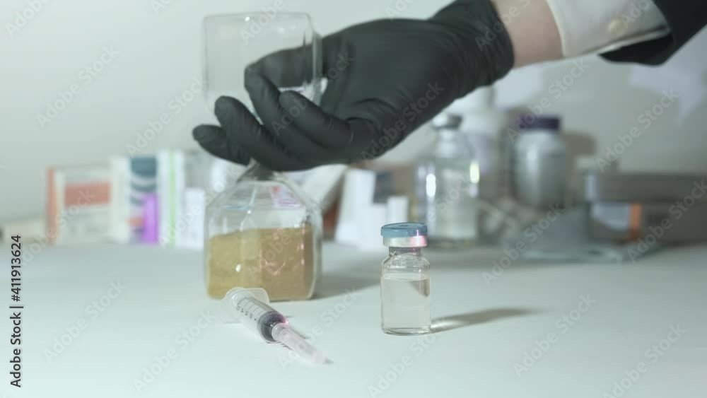 Man hand in glove against virus turns over hourglass. In foreground vaccine and syringe. Concept of deadline vaccination during epidemics, pandemics Man hand in glove against virus turns over hourglass. In foreground vaccine and syringe. Concept of deadline vaccination during epidemics, pandemics