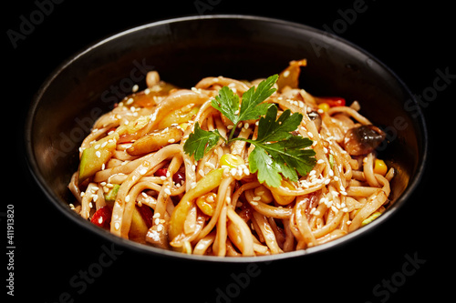 wok noodles with vegetables greens and sesame seeds in a plate on a black background