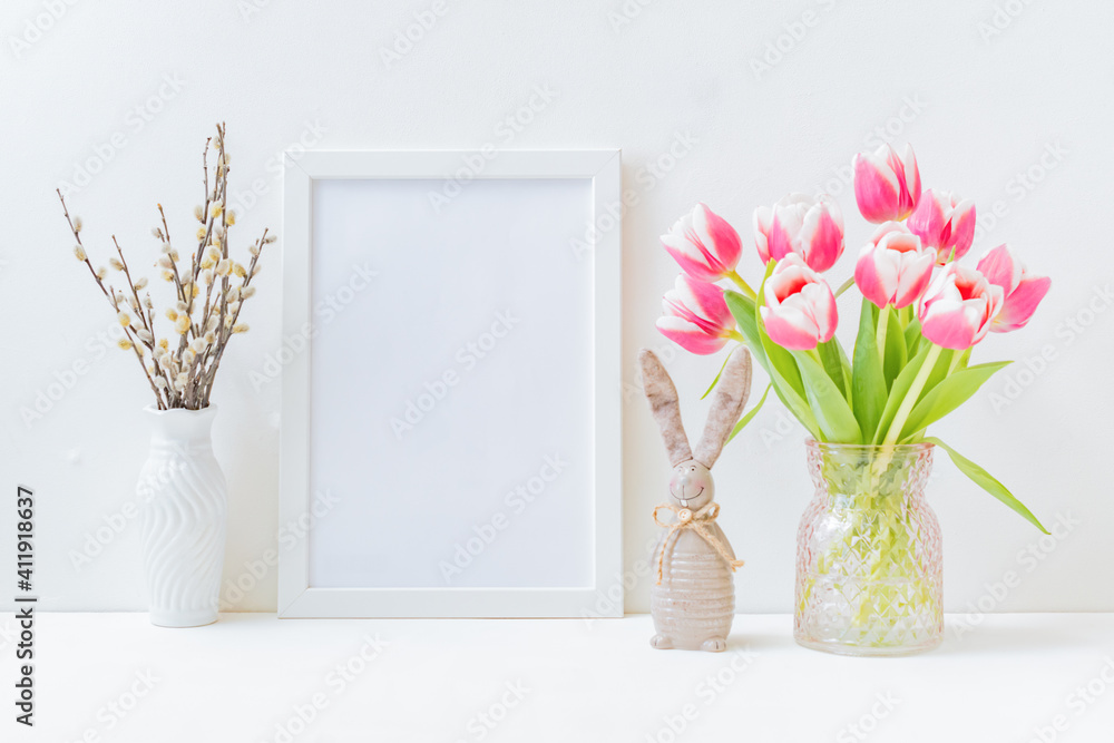 Home interior with easter decor. Mockup with a white frame and willow branches, pink tulips in a vase on a light background Home interior with easter decor. Mockup with a white frame and willow branches, pink tulips in a vase on a light background