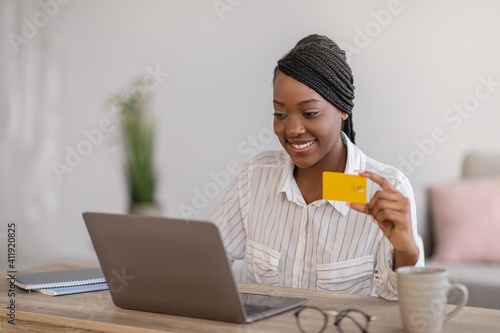 Smiling african woman freelancer holding credit card, working on laptop