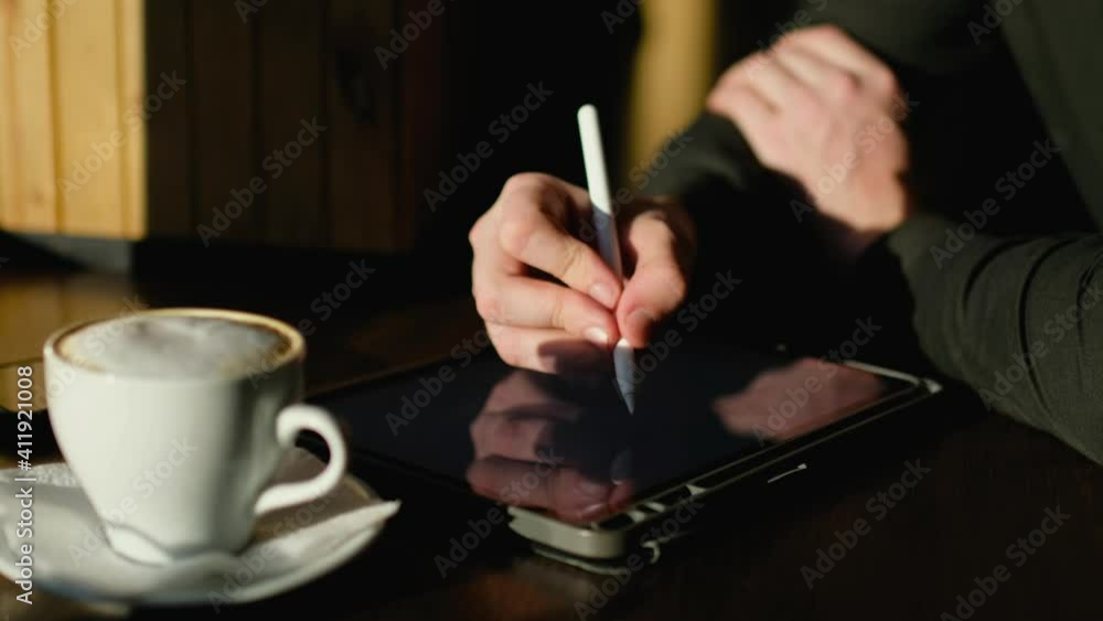 Close-up of a hand working on a tablet with a stylus. Close-up of a hand working on a tablet with a stylus.