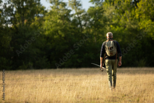 Man with backpack and fly fishing pole walking in rural field