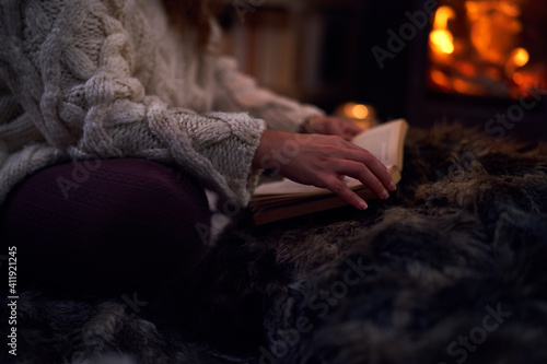 Woman reading book on blanket at cozy fireside