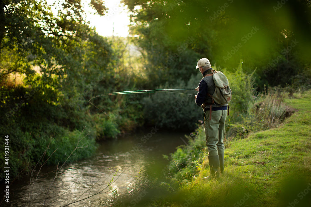 Man with backpack fly fishing at riverbank Man with backpack fly fishing at riverbank