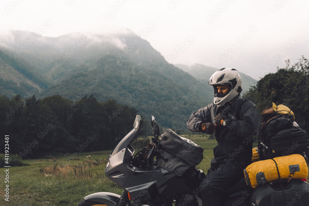 A motorcycle driver with motorbike, Adventure vacation, biker dressed in raincoat. sealed bag, water resistant, overalls. Mountains road trip, side bags equipment. copy space