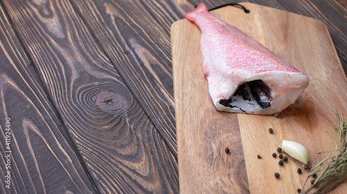 Fresh and ready to cook raw pink Perch fish with ingredients like lemon and carrot on a wooden pad, selective focus.