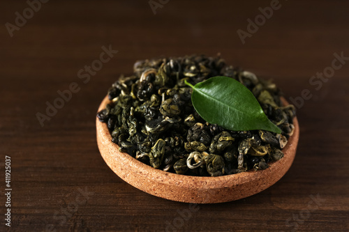 Dried green tea leaves in cork bowl on wooden table, closeup
