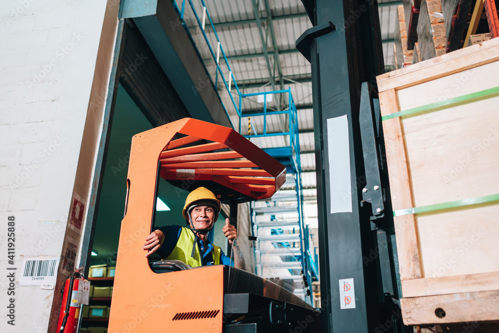 Fototapeta premium Worker driver asian man in protective safety jumpsuit uniform with yellow hardhat at warehouse forklift loader works