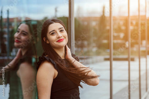 Portrait of a latin woman  smiling  with a friendly expression  with an glass building in the background. Job  economy and businesswoman concept