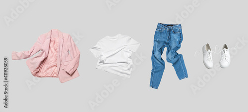 Fotografie White flying cotton T-shirt, blue jeans, white leather sneakers, fashionable pink blazer jacket isolated on gray background