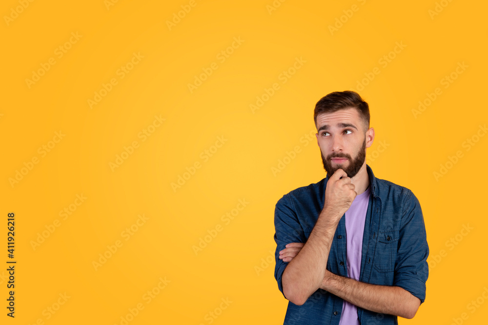 Portrait of attractive young guy thinking and touching his chin over orange studio background, copy space Portrait of attractive young guy thinking and touching his chin over orange studio background, copy space