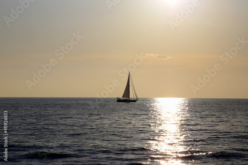 Sailboat on the horizon backlit with the ray of sun setting over the sea