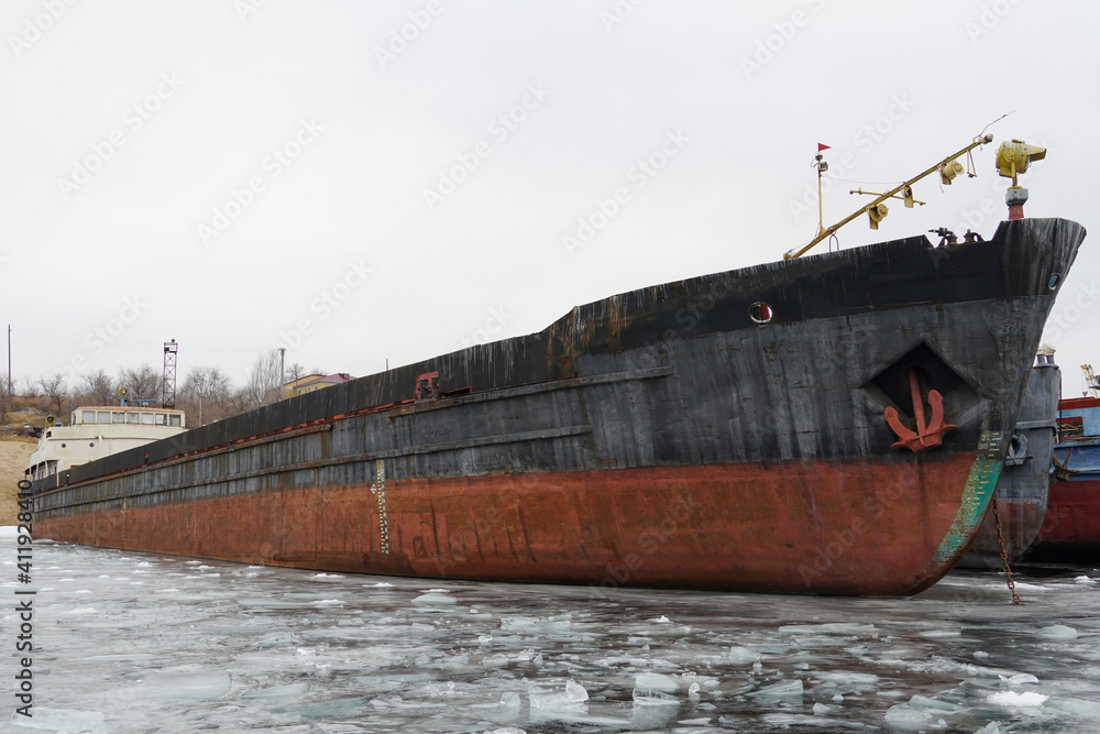 Fototapeta premium Old rusty motor ship. Wintering ships on a frozen river in their port. Volgograd. Russia