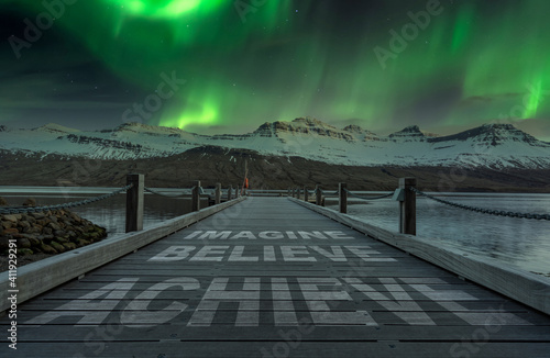 imagine believe acheive text quote written on wooden dock. Beautiful landscape scenery in the background with aurora borealis dancing above. photo
