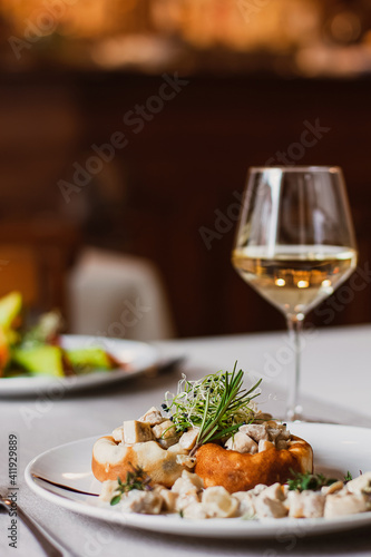 Stuffed mushrooms filled with cheese, mushroom stem and microgreen on the white plate with a glass of wine