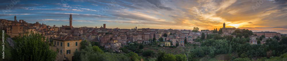 Panorama of Siena old town at sunrise, a medieval and Renaissance city in Tuscany, Italy, with Mangia tower, church, old houses and palaces on a green hill
