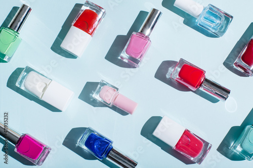Bottles of colorful nail polish on pastel blue and pink background. Manicure and pedicure concept. Flat lay, top view, copy space.