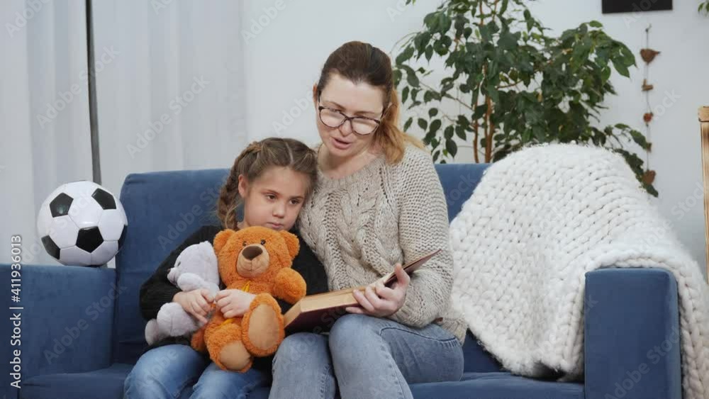 mom reads a book to her lockdown daughter at home. kid dream coronavirus stay home concept. mom is sitting on the couch with her daughter reading a book. mother and daughter happy family mom reads a book to her lockdown daughter at home. kid dream coronavirus stay home concept. mom is sitting on the couch with her daughter reading a book. mother and daughter happy family