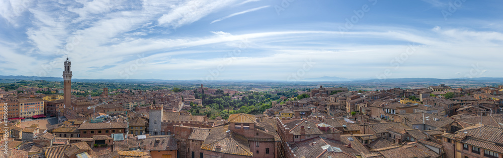 Panorama of Siena old town at sunrise, a medieval and Renaissance city in Tuscany, Italy, with Mangia tower and piazza del Campo, a church, old houses and palaces on a green hill