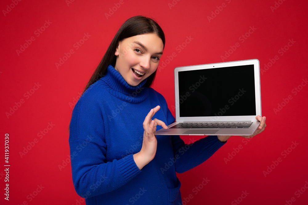 Naklejka premium Photo of beautiful young woman holding computer laptop looking at camera isolated over colourful background