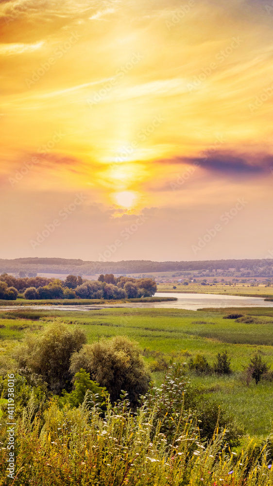 Summer landscape with picturesque sky at sunset on a meadow with trees and river