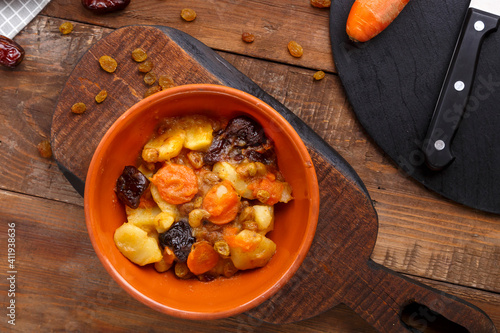 Jewish cuisine dish sweet tsimes with carrot dates in a clay plate on a wooden board. photo