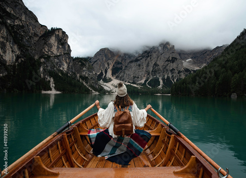 Happy tourist woman with hat sitting in a wooden boat on Braies lake surrounded by the mountains of the Italian Alps  © marina