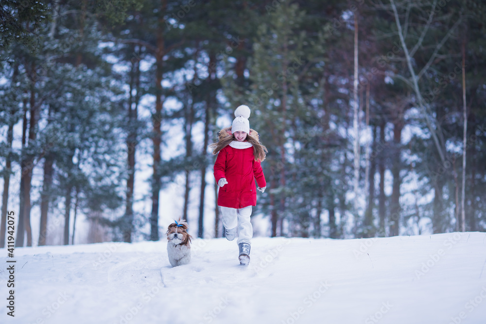 Lovely joyful girl running with a dog in the winter forest