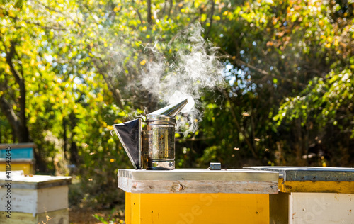 Bee smoker stands on yellow beehive. Steel instrument for pouring smoke in air. Apiculture concept. © Vadim