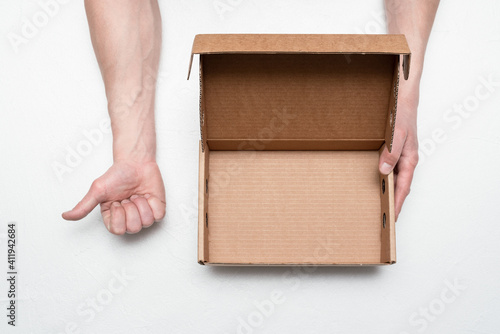 Empty cardboard box with copy space in the male hand and thumbs up gesture by the hand on the gray background. Recommend service. © Natali