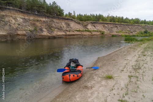 Stop for a kayak on the low bank. It's raining. The river makes a turn. There is a backpack and a tent on the kayak. Solo hike.
