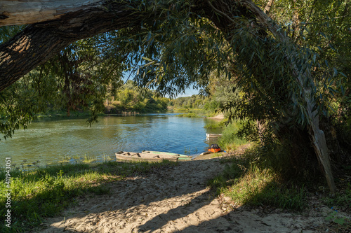 Wooden boats and a kayak docked. Descent to the entrance near the trees. Old mill on the Khopyor river. Destroyed dam and building. August on the river. Rafting and travel. Descent downstream.