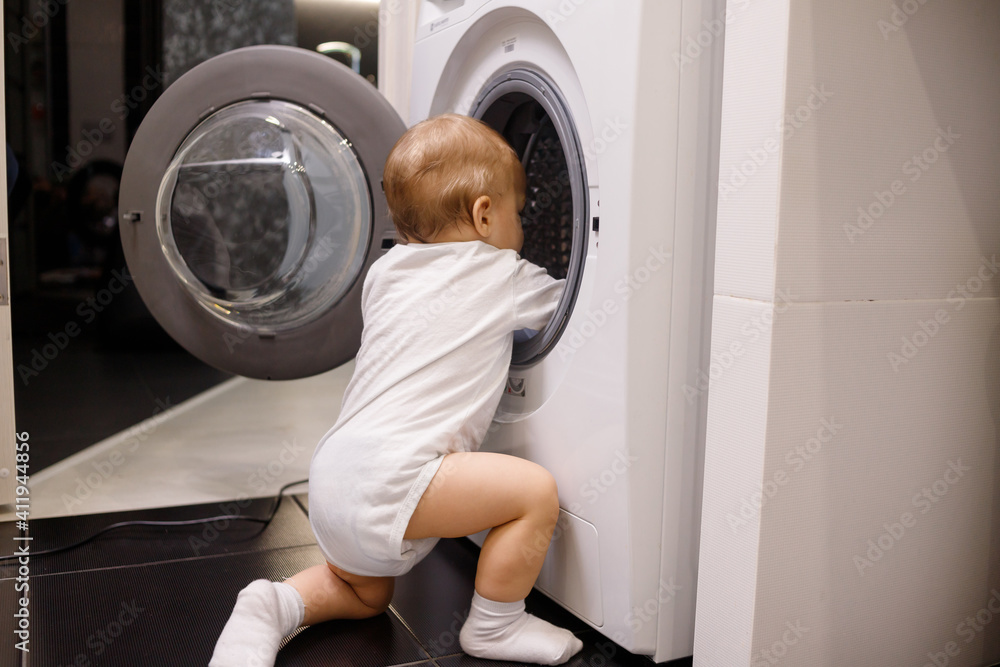Child climbing into front-loading washing machine. Side view. Lack of parental supervision Child climbing into front-loading washing machine. Side view. Lack of parental supervision