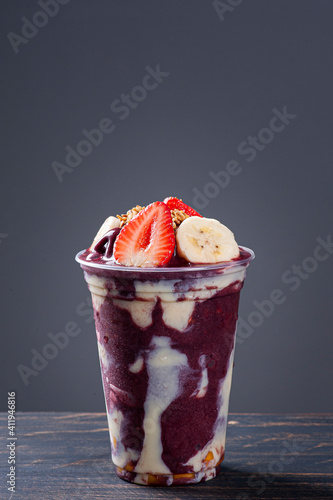 Brazilian frozen açaí in a plastic cup with condensed milk, banana and strawberry. Fruit from the Amazon. Copy space