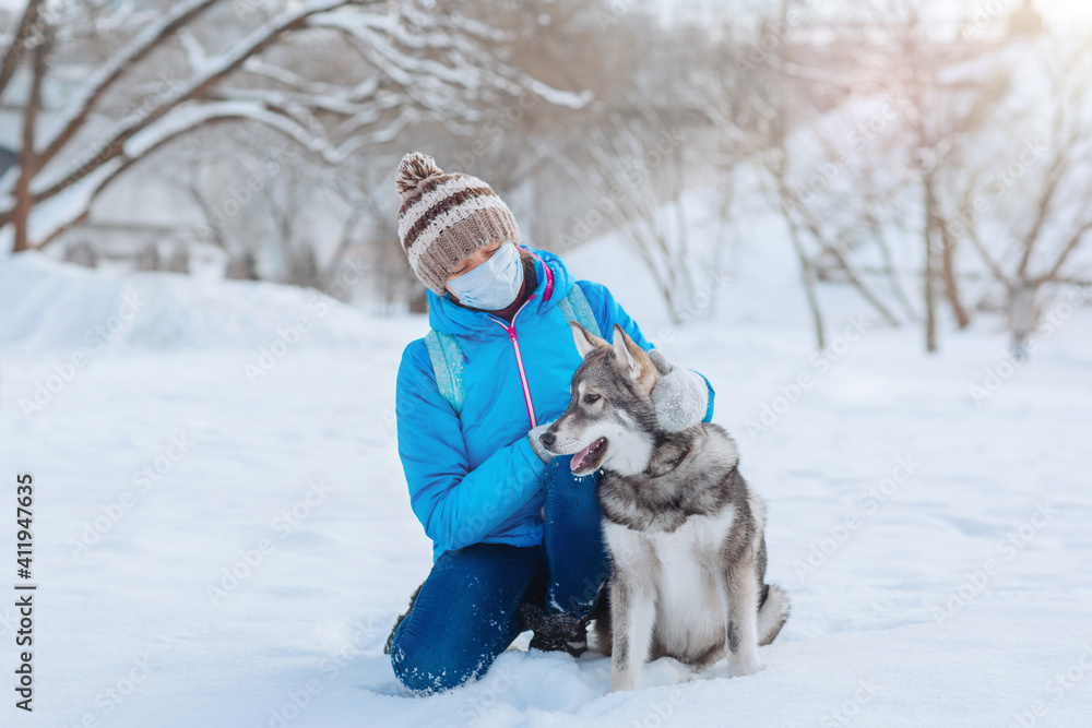Alone woman wearing a protective mask walks with her dog in the winter outdoors due to the covid-19 coronavirus Alone woman wearing a protective mask walks with her dog in the winter outdoors due to the covid-19 coronavirus