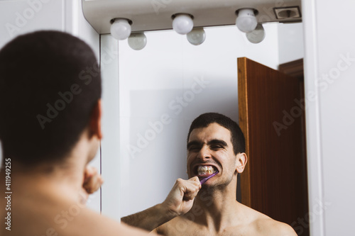 
young man brushing his teeth with a toothbrush in the bathroom at home photo