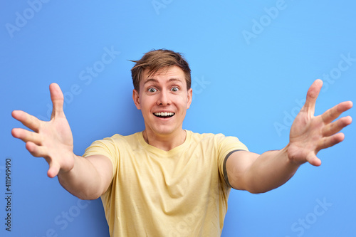 male spread arms, going to hug, smiling at camera, expressing positive emotions, gesturing. isolated blue background photo