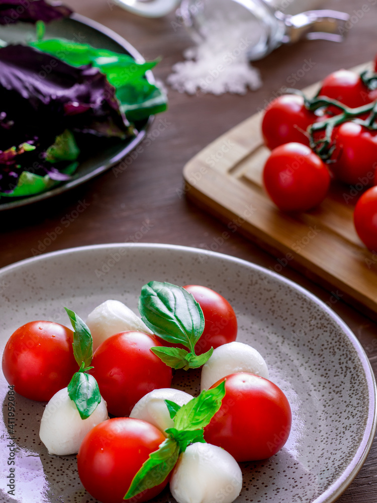 Caprese salad on round plate. Round tomatoes, mini mozzarella and green basil. Caprese salad on round plate. Round tomatoes, mini mozzarella and green basil.