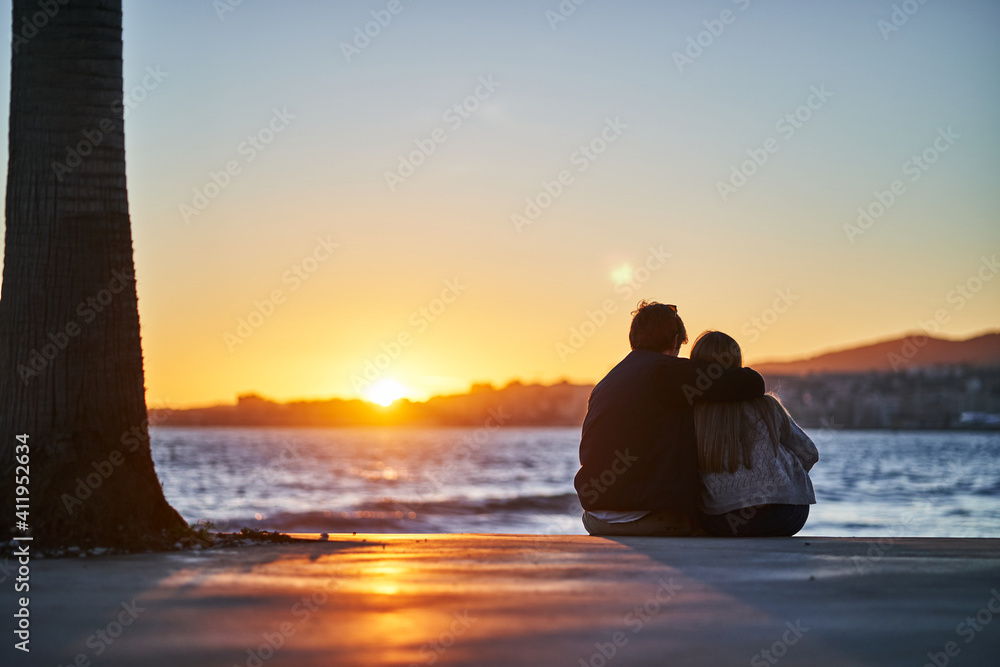 Lovely unrecognizable couple enjoying sunset near sea