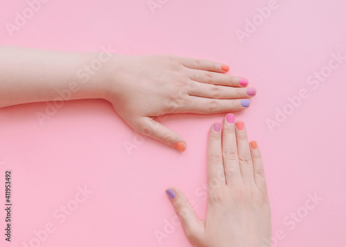 Colored manicure Top view photo with copy space Female hands with multicolored nails on light pink background