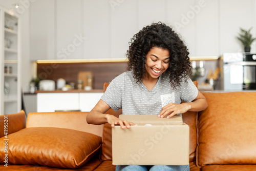 Принти на полотні Positive young African American woman sitting on the couch with carton box on la