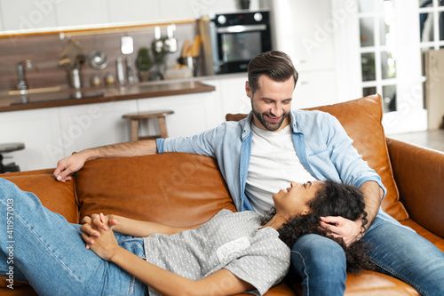 Canvas Print Interracial couple chilling on the couch in the studio apartment, smiling and lo